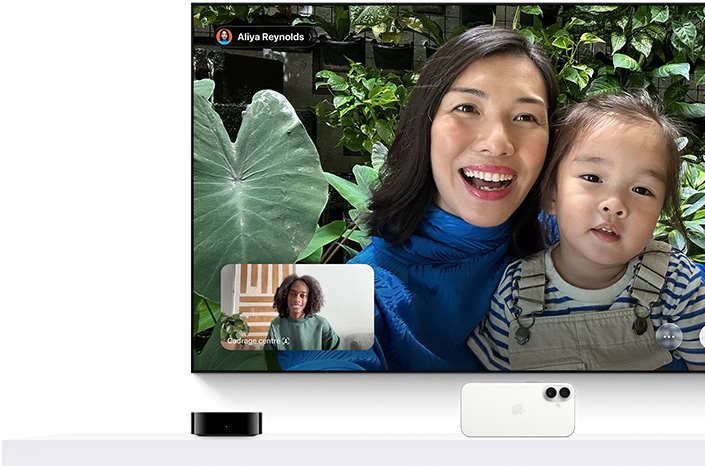 Apple TV 4K et iPhone : un écran de télévision affiche un appel FaceTime, une personne tient une petite fille dans ses bras, une deuxième personne est visible dans une petite fenêtre