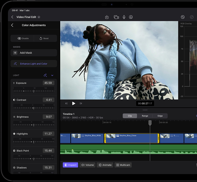 Un iPad Pro, parte frontal, marco de la pantalla negro, la pantalla muestra una app de edición de video con una foto de una persona modelando un polerón azul y pantalones blanco con negro, el panel de ajuste de color está abierto a la izquierda con varios efectos de video y reguladores, línea de tiempo en la parte inferior con múltiples clips de video y pistas de audio