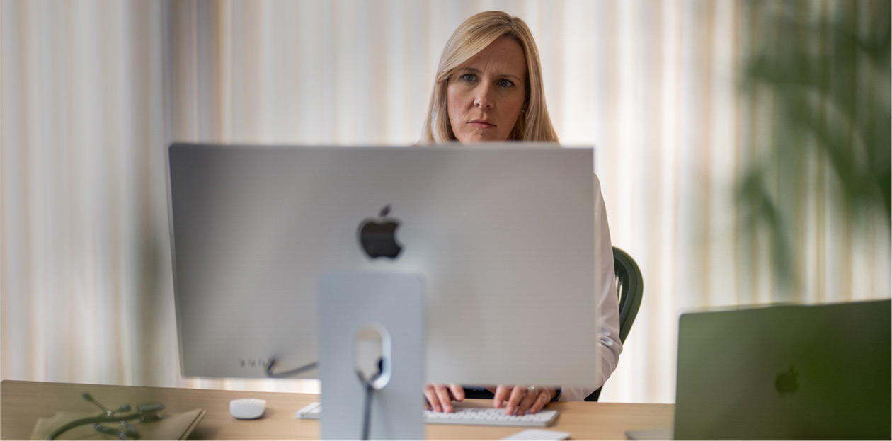 Una profesional sanitaria mira la pantalla de un iMac en su escritorio.