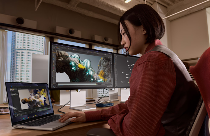 บุคคลหนึ่งขณะทำงานในออฟฟิศโดยมี MacBook Pro เชื่อมต่ออยู่กับ Studio Display XDR