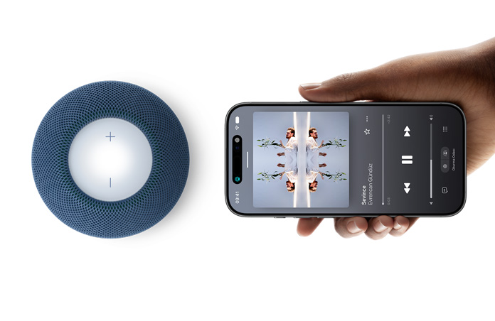 HomePod mini 2 ve iPhone: Bir el, handoff özelliği için mavi renk HomePod mini 2’nin yanında bir iPhone’u yatay olarak tutuyor
