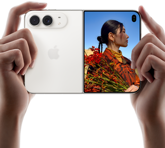 iPhone Duo, колір «біла зоря», тримають двома руками в горизонтальному положенні, розкладений; на лівій панелі видно систему двох камер Fusion із роздільною здатністю 48 МП, а на правій — людину, яку фотографують на зовнішньому дисплеї; об’єкт зйомки може бачити своє обличчя під час фотографування за допомогою режиму Duo Preview