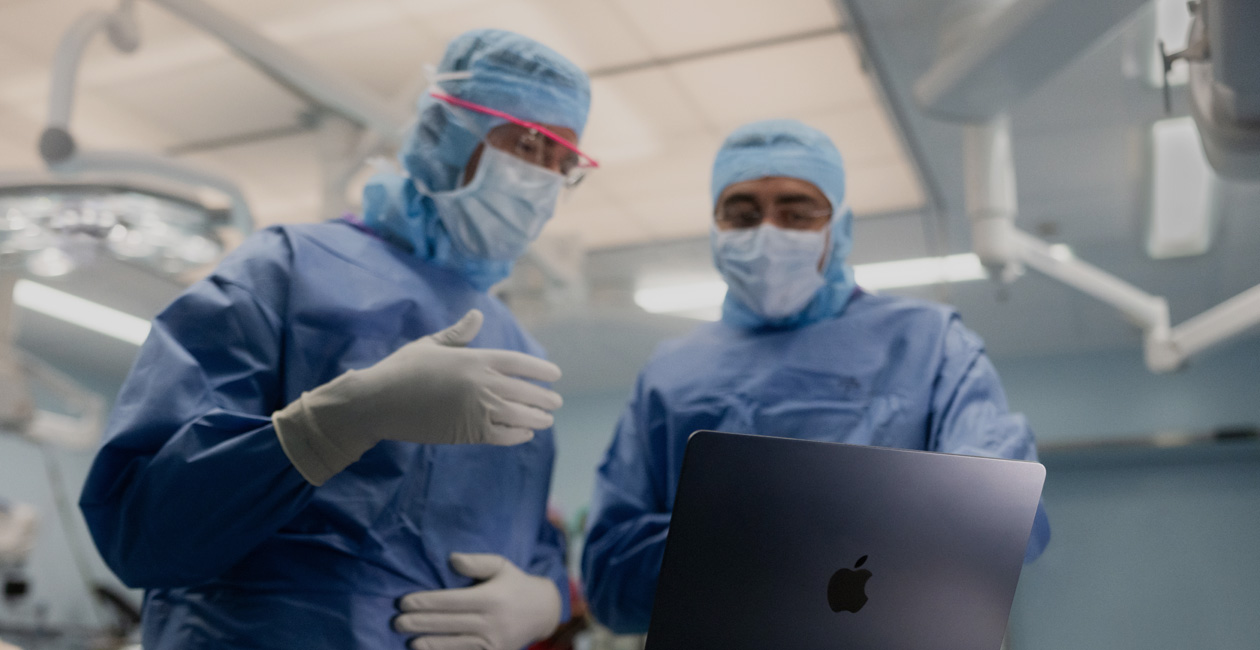 Zwei Chirurgen im OP sprechen über die Inhalte auf dem Display eines MacBook Pro.