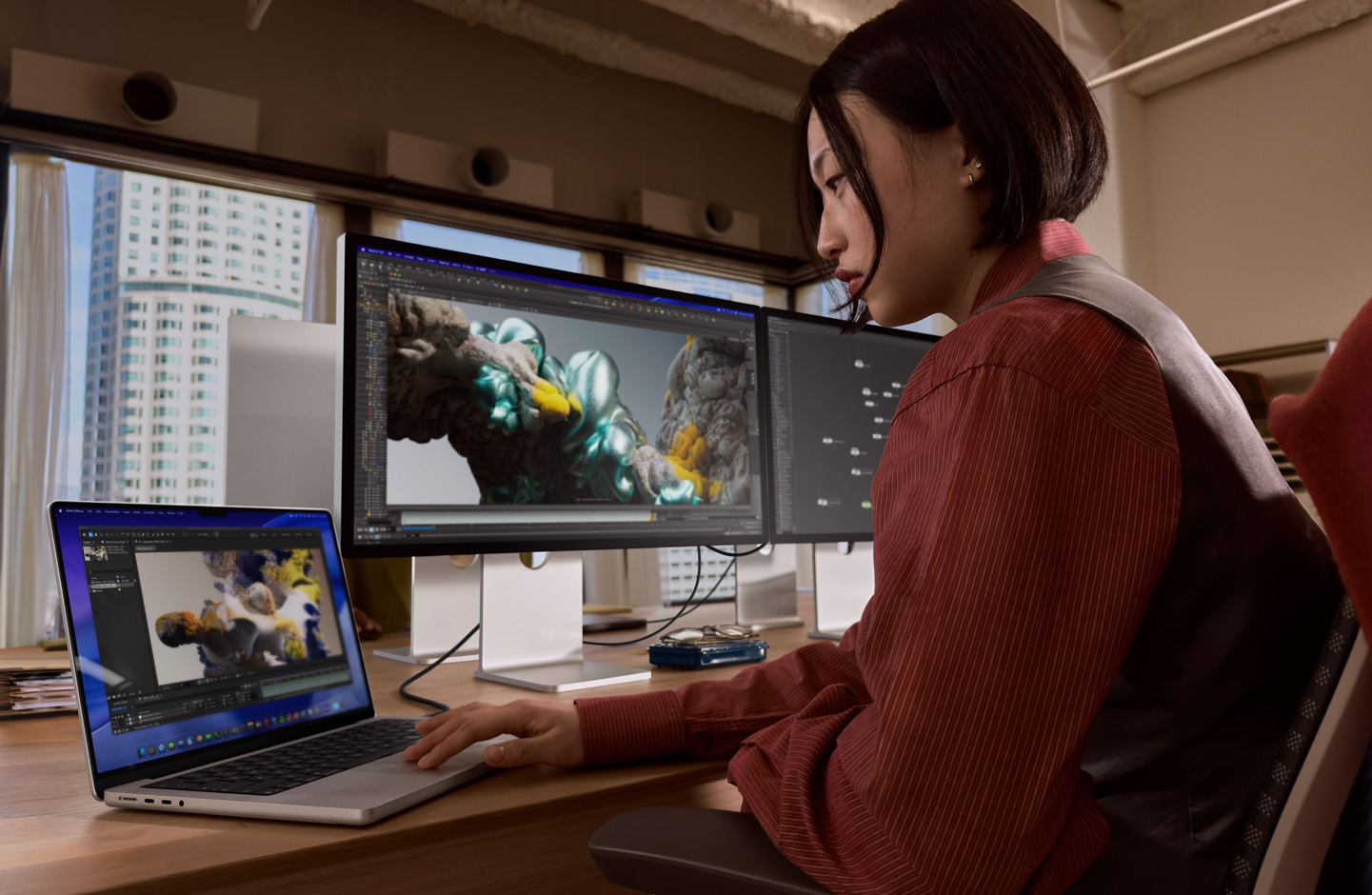 Una persona en una oficina trabaja en una laptop MacBook conectada a un monitor Studio Display XDR mediante un puerto Thunderbolt 5