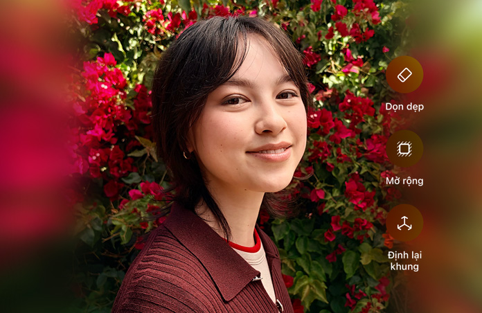 Photo of smiling person with brown hair, wearing a brown sweater, surrounded by red flowers, AI photo editing demo with Clean Up, Extend, Reframe options shown over photo